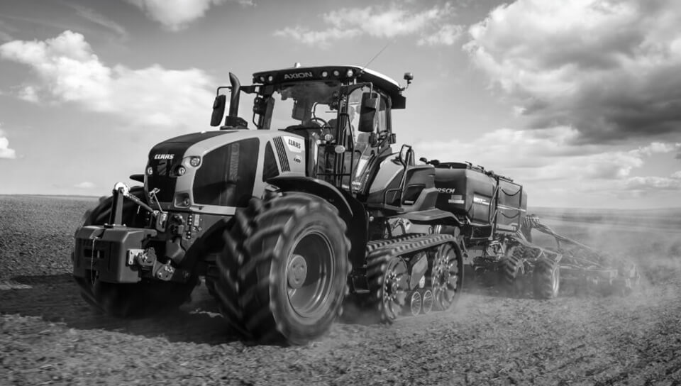 A modern tractor works a vast farmland under a cloudy sky.