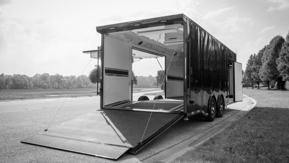An open cargo trailer with a ramp parked by a roadside.
